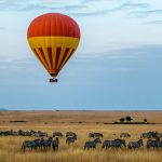 A hot air balloon drifting low over the savannah at sunrise