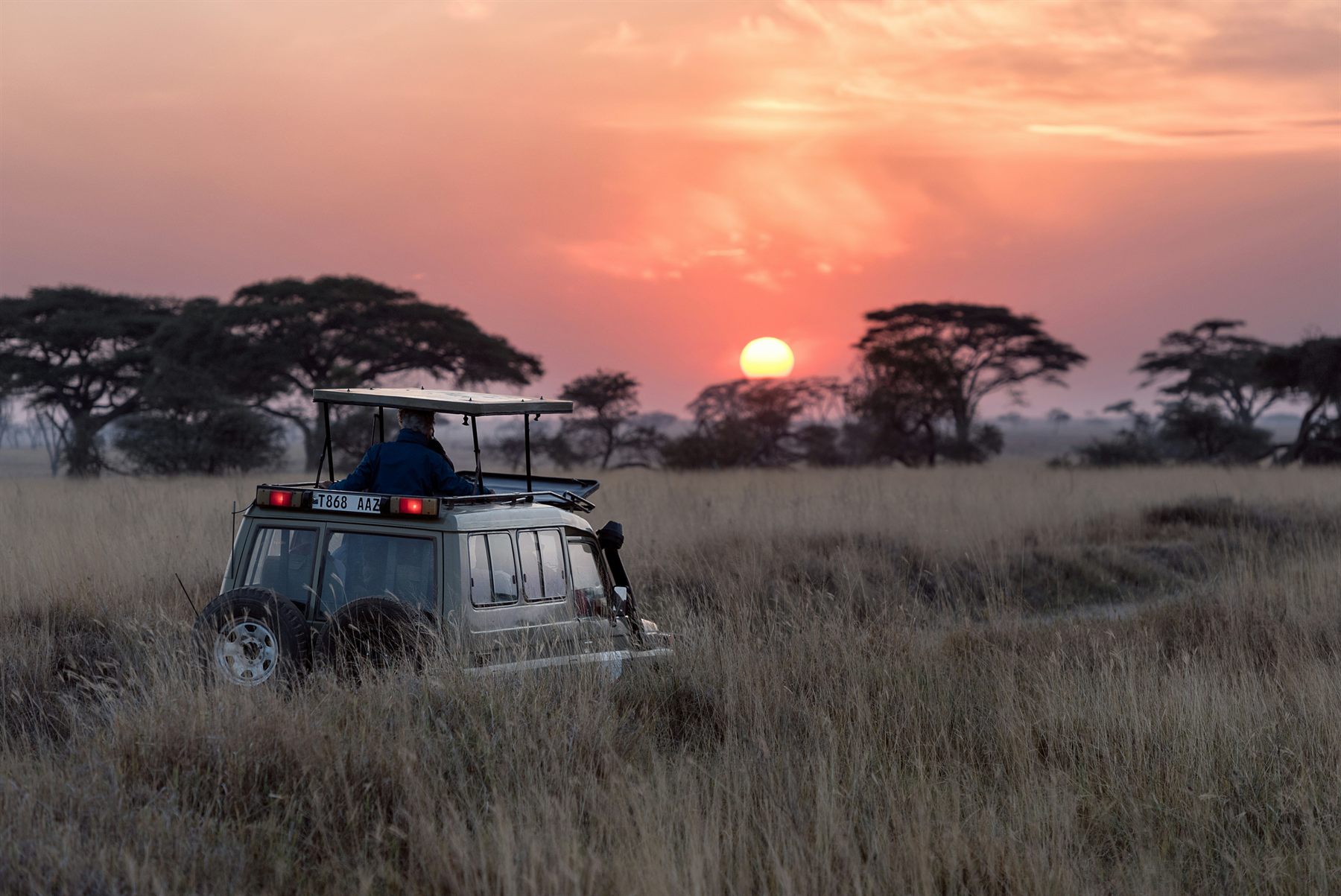 A safari vehicle travelling a dirt road across wide open country